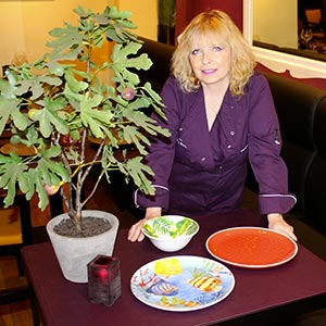Photo de Karin Burton posant à coté des assiettes en mélamine des jardins de la comtesse au restaurant Lou Ferri